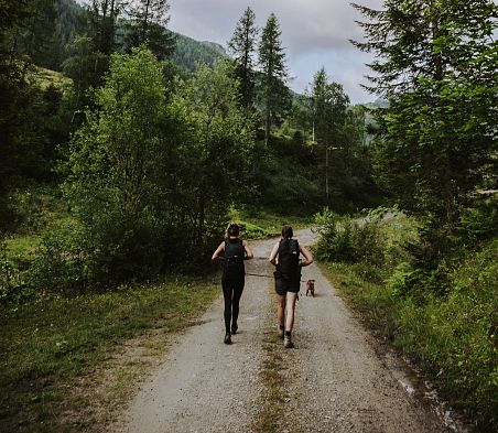 Zwei Wanderinnen sind mit ihrem Hund im Wald in Flachau unterwegs.