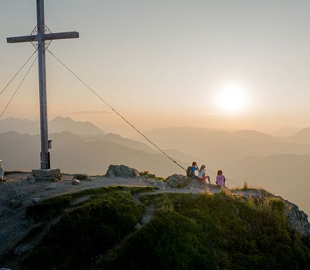 Sonnenaufgangstour auf den Gipfel des Grießenkarecks in Flachau, Salzburgerland. Drei Personen haben den Anstieg schon geschafft und genießen den Blick auf das Panorama vor ihnen.