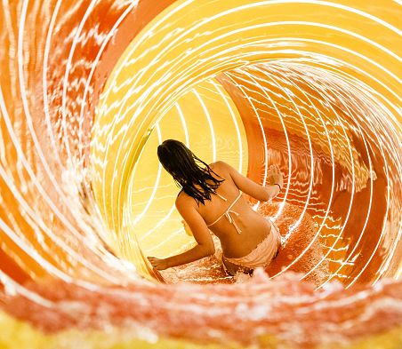 Eine Besucherin gleitet durch die beleuchtete Röhrenrutsche ins Wasser.