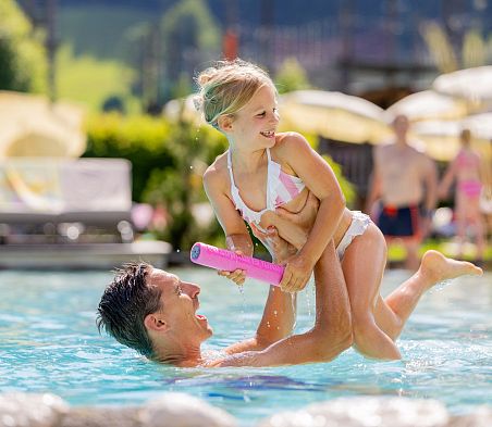 Kind spielt mit einer Wasserpistole im Pool in Flachau, Erwachsener hält es im Wasser.