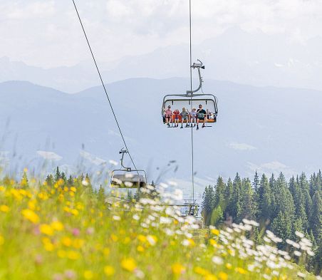 Kinder und Eltern fahren mit der Sommerbergbahn über Almwiesen in Flachau mit Blick auf die Alpen.