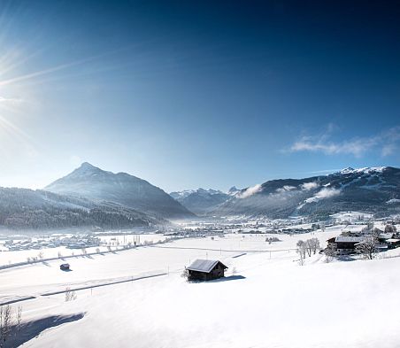 Schöne Winterlandschaft mit Blick auf Berge, Pisten und verschneite Huetten in Flachau
