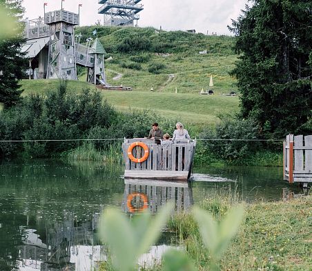 Familie fährt auf Floß über Geistersee mit Geisterschloss im Hintergrund