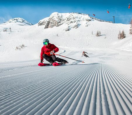 Nahaufnahme einer frisch präperierten Piste und einem Skifahrer mit roter Jacke in Zauchensee.