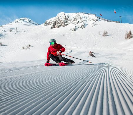 Nahaufnahme einer frisch präperierten Piste und einem Skifahrer mit roter Jacke in Zauchensee.