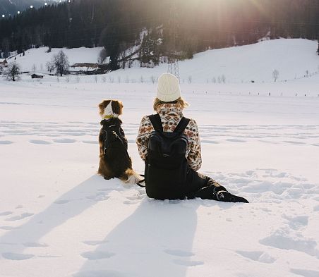 Person und Hund sitzen im Schnee mit Blick auf Sonnenuntergang in Flachau, Salzburger Land.