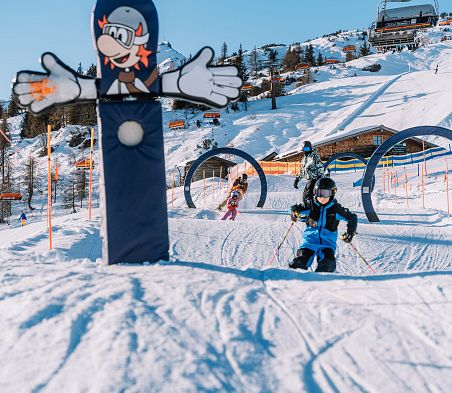 Kinder fahren durch Ski-Parcours in Flachau. Im Hintergrund erkennt man die Hofalm und den Starjet 3.