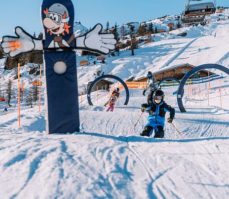 Kinder fahren durch Ski-Parcours in Flachau. Im Hintergrund erkennt man die Hofalm und den Starjet 3.