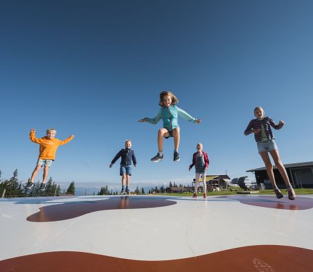 Kinder springen am Hüpfkissen einer Spielstation von Wagraini's Grafenberg.
