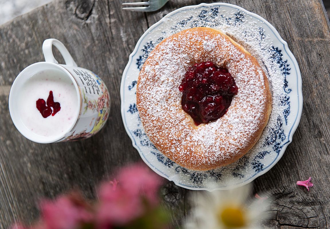 Ein Bauernkrapfen und eine Tasse mit frischer Buttermilich, jeweils gefüllt mit Preiselbeermarmelade.