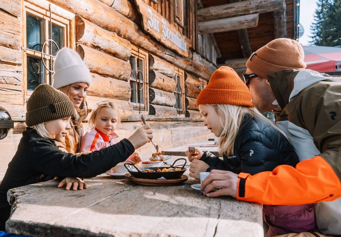 Eine Familie mit drei Kindern genießt das gute Essen auf einer traditionellen Hütte in Flachau, Salzburgerland.