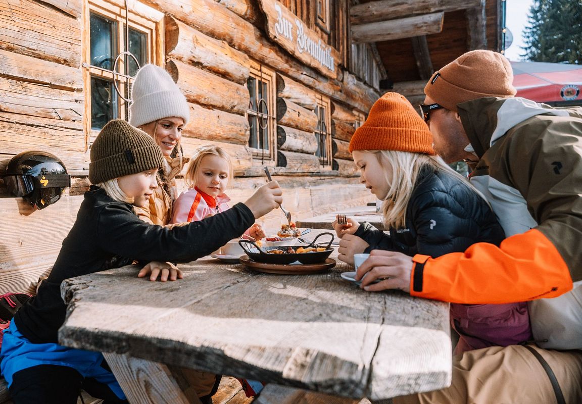 Eine Familie mit drei Kindern genießt das gute Essen auf einer traditionellen Hütte in Flachau, Salzburgerland.