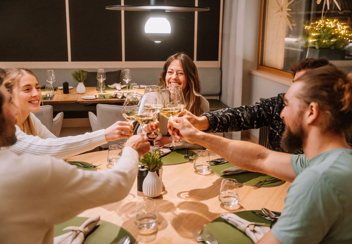 Freunde stoßen beim gemeinsamen Abendessen in Flachau mit einem schönen Glas Wein an.