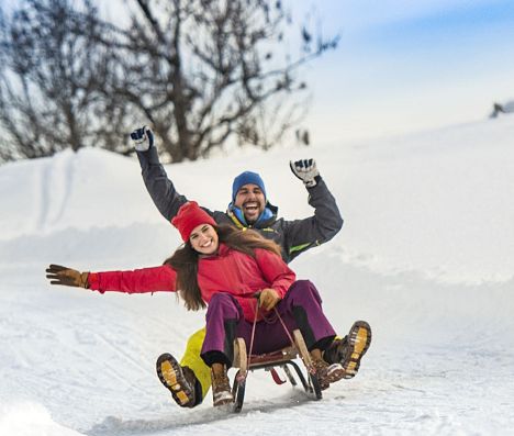 Zwei Frauen und ein Mann sausen auf Schlitten die Rodelbahn in Flachau hinunter.