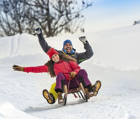 Zwei Frauen und ein Mann sausen auf Schlitten die Rodelbahn in Flachau hinunter.