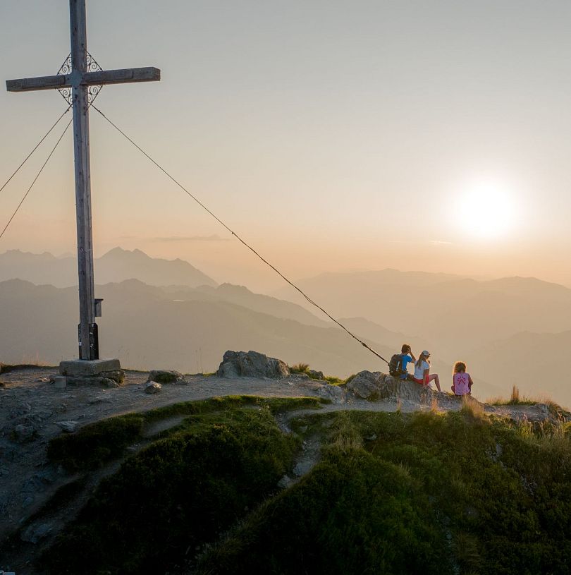 Sonnenaufgangstour auf den Gipfel des Grießenkarecks in Flachau, Salzburgerland. Drei Personen haben den Anstieg schon geschafft und genießen den Blick auf das Panorama vor ihnen.