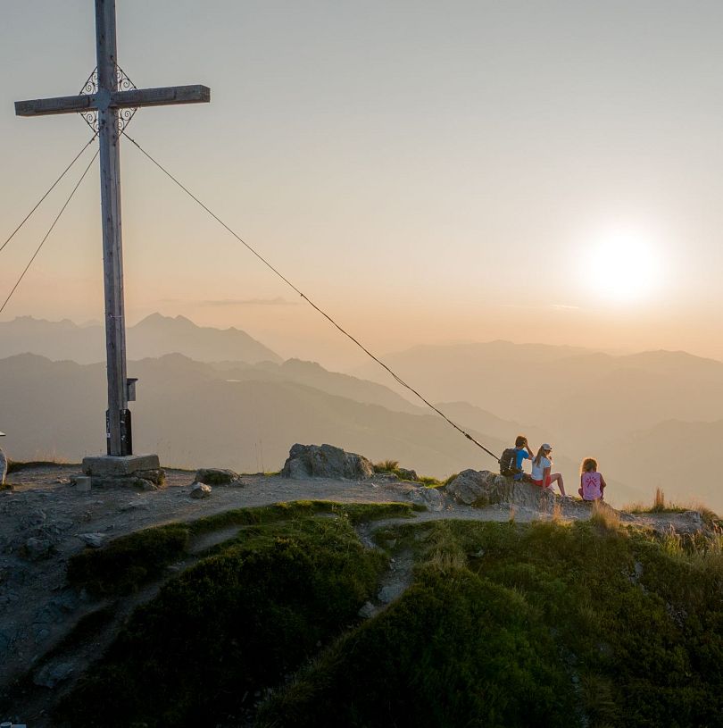 Sonnenaufgangstour auf den Gipfel des Grießenkarecks in Flachau, Salzburgerland. Drei Personen haben den Anstieg schon geschafft und genießen den Blick auf das Panorama vor ihnen.