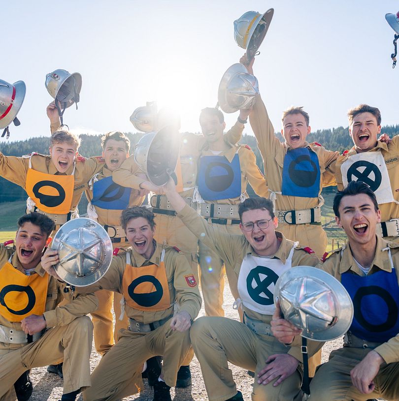 10 junge Männer in Feuerwehr-Montur machen ein Gruppenbild und halten ihre Helme in die Luft.