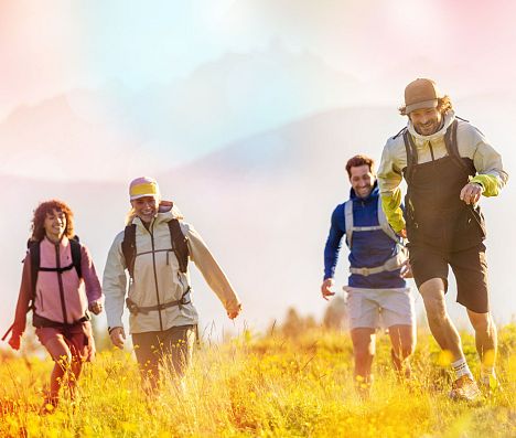 Zwei Frauen und zwei Männer beim Wandern in Flachau auf einer Wiese. Ein Mann rennt voraus. Das Bild hat einen farbigen Filter.