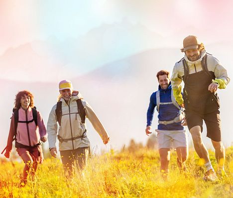 Zwei Frauen und zwei Männer beim Wandern in Flachau auf einer Wiese. Ein Mann rennt voraus. Das Bild hat einen farbigen Filter.