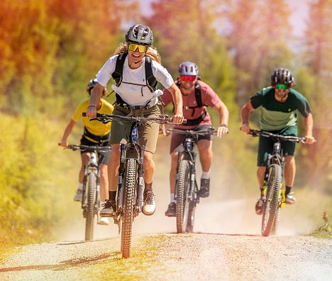 Vier Mountainbiker fahren auf einer Schotterstraße in Flachau, Salzburgerland den Berg hinauf.