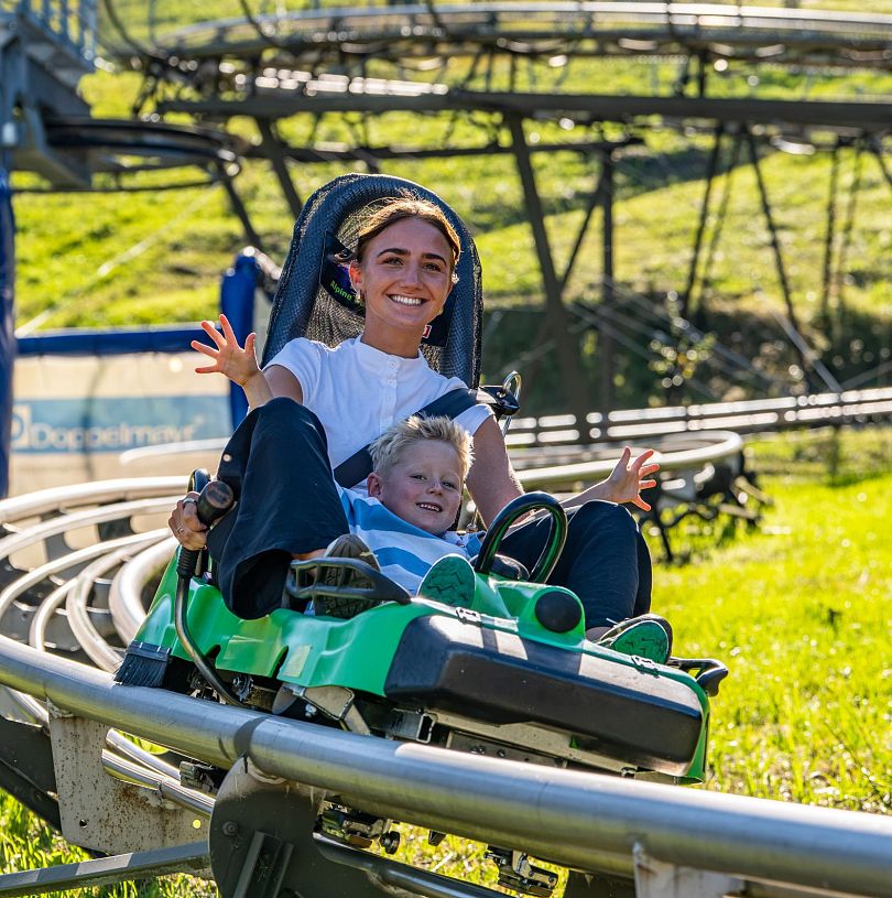 Frau und Kind fahren gemeinsam mit die Allwetterrodelbahn Lucky Flitzer in Flachau hinunter.