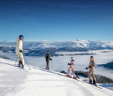 Vier Skifahrer auf einer präparierten Piste mit weitem verschneitem Alpenpanorama in Flachau.