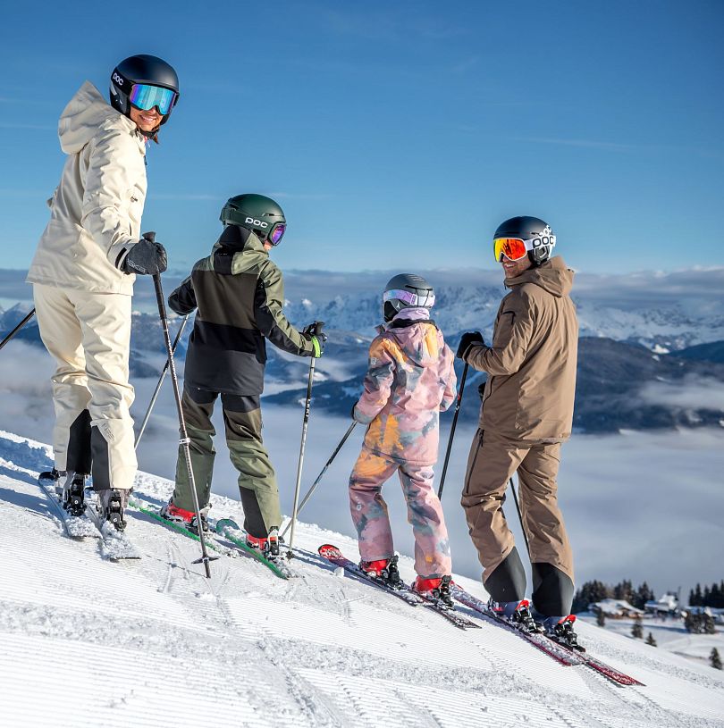 Familie mit zwei Kindern auf Skiern vor dem verschneiten Bergpanorama in Flachau.