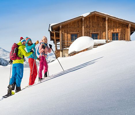 Drei Schneeschuhwanderer  nähern sich einer verschneiten Berghütte – Naturerlebnis in Flachau, Salzburger Land.