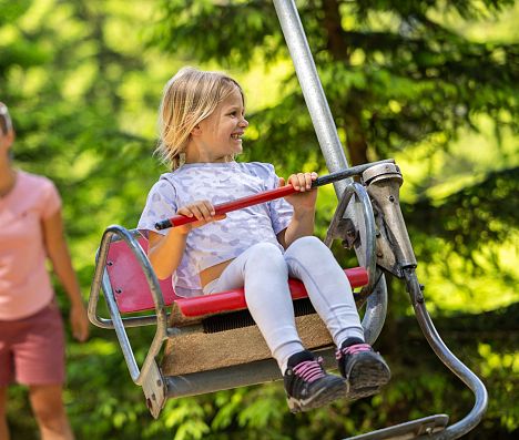Kind fährt mit einer Seilbahn auf einem Spielplatz in Flachau im SalzburgerLand, im Hintergrund eine erwachsene Person.