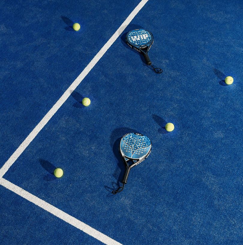 Padel-Schläger und mehrere Bälle liegen auf einem blauen Court.