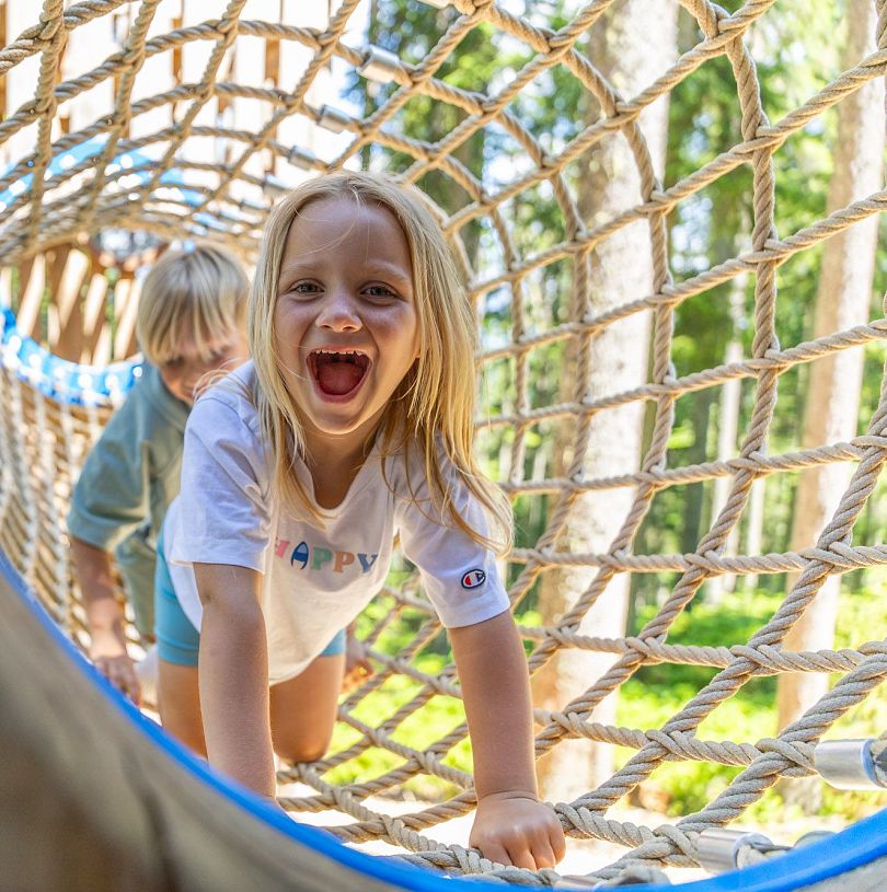 Zwei Kinder krabbeln lachend durch ein Kletternetz im Waldseilgarten in Flachau.