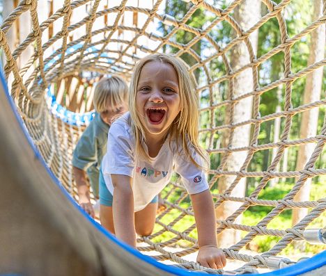 Zwei Kinder krabbeln lachend durch ein Kletternetz im Waldseilgarten in Flachau.