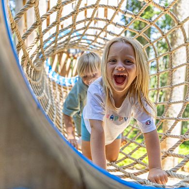 Zwei Kinder krabbeln lachend durch ein Kletternetz im Waldseilgarten in Flachau.