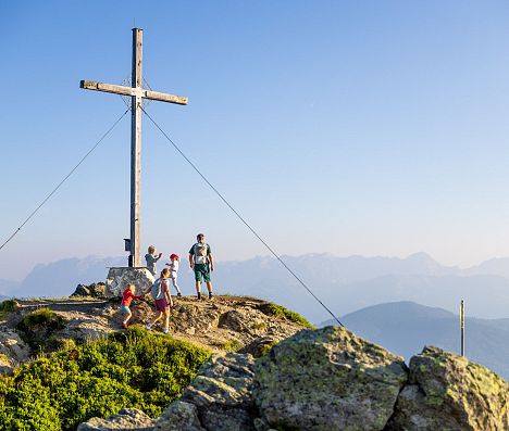 Familie erreicht einen Gipfel mit Gipfelkreuz in Flachau und genießt das Panorama der Salzburger Alpen.