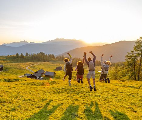 Gruppe von Wanderern springt bei Sonnenuntergang auf einer Alm in Flachau mit Blick auf die Alpen.