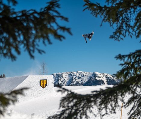 Snowboarder fliegt über Kicker im Absolut Park Flachau in Ski amadé, eingerahmt von verschneiten Bäumen.