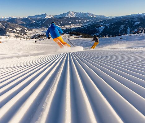 Zwei Skifahrer carven auf präparierter Piste in Flachau, Ski amadé, mit Alpenpanorama im Salzburger Land.
