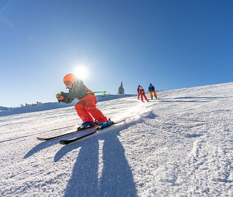 Skifahrer in Rot führt Gruppe auf sonniger Piste in Flachau, Ski amadé im Salzburger Land an.