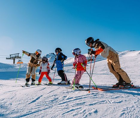 Familie steht in Skiausrüstung etwas unterhalb der Bergstation Starjet 3 und bereitet sich auf die Abfahrt vor.