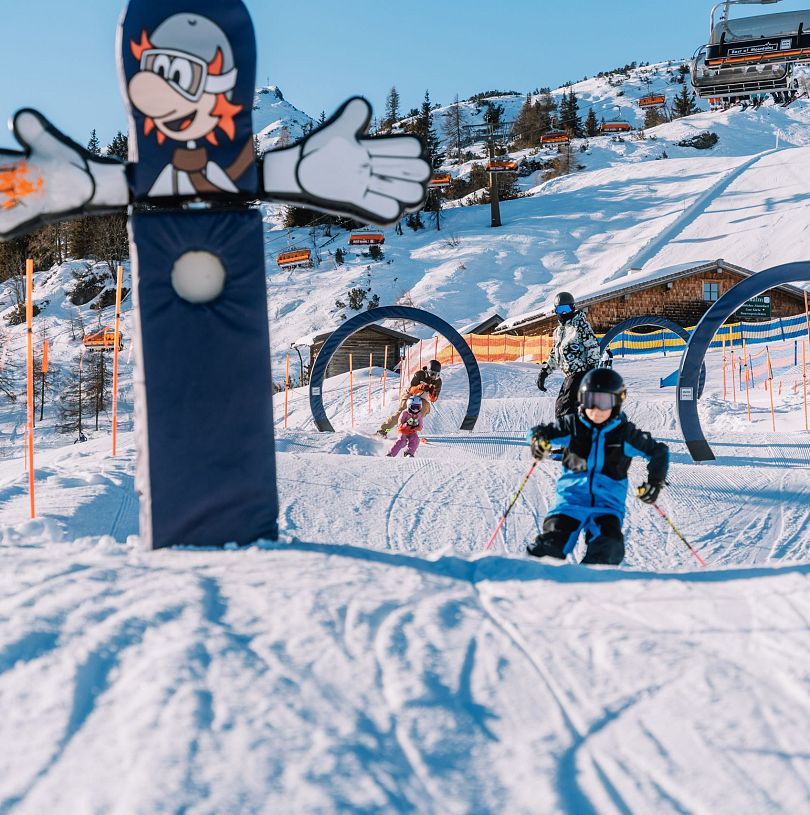 Kinder fahren durch Ski-Parcours in Flachau. Im Hintergrund erkennt man die Hofalm und den Starjet 3.
