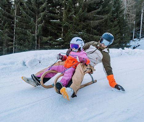 Vater und Tochter sind rasant auf ihrem Schlitten ins Tal hinunter unterwegs.