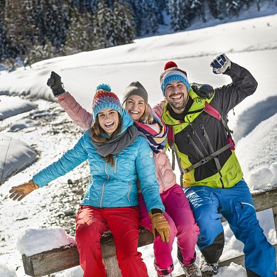 Drei Freunde posten an ein Brückengelände angelehnt und genießen die herrliche Winterlandschaft im Flachautal.