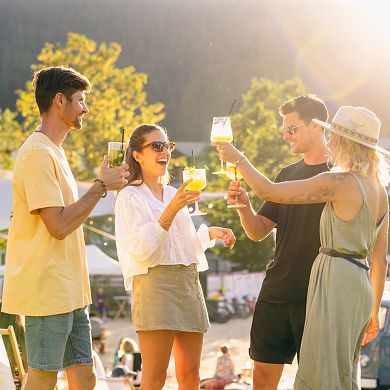 Zwei Männer und zwei Frauen stoßen bei einer Veranstaltung in Flachau mit Getränken an. Im Hintergrund leuchtet die Sonne an einem warmen Sommertag.