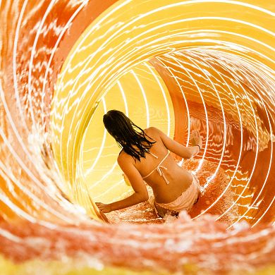 Eine Besucherin gleitet durch die beleuchtete Röhrenrutsche ins Wasser.