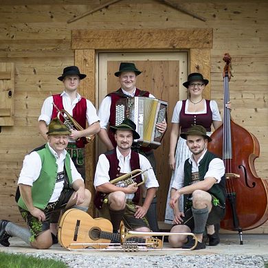 Die Hallgrafen Musikanten in Tracht mit Instrumenten vor einer Holzhütte.