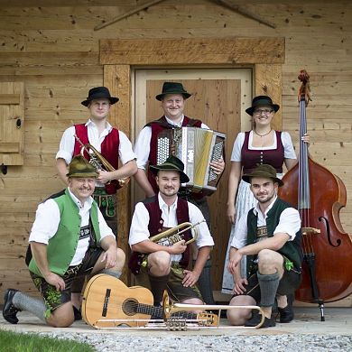Die Hallgrafen Musikanten in Tracht mit Instrumenten vor einer Holzhütte.