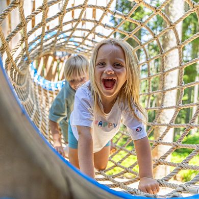 Zwei Kinder krabbeln lachend durch ein Kletternetz im Waldseilgarten in Flachau.
