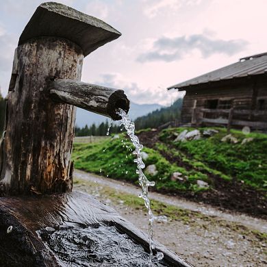Holzbrunnen mit glasklarem, erfrischendem Quellwasser vor einer Almhütte in Flachau.