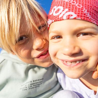 Zwei Kinder lachen und umarmen sich beim Familienurlaub in Flachau vor blauem Himmel.